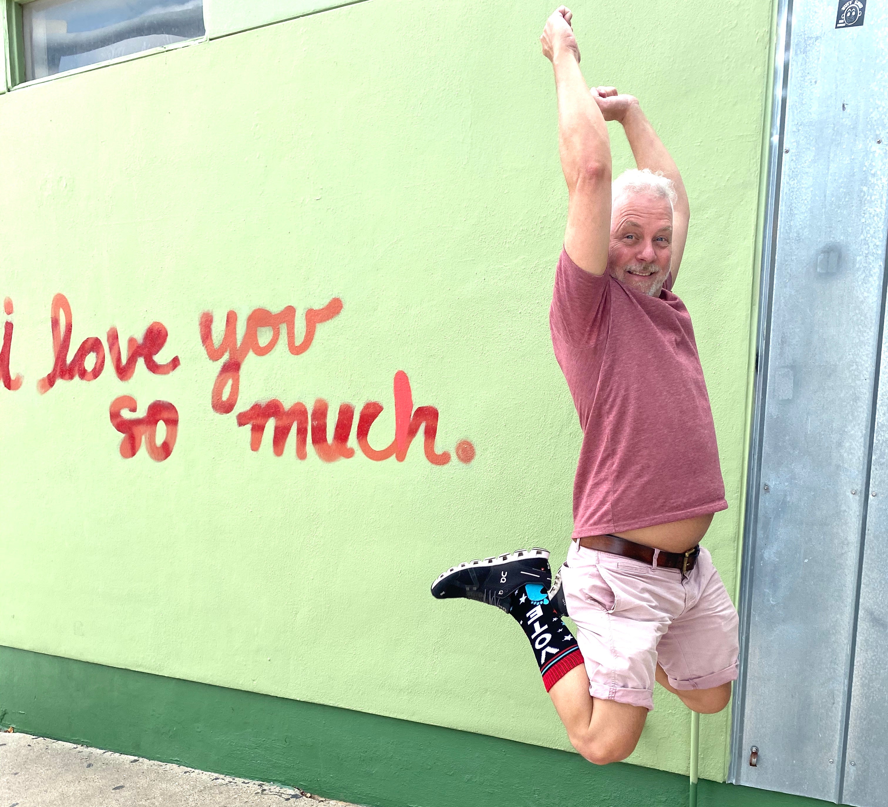 White man jumps up wearing SoleMate Sox in front of Jo's Coffee I love You So Much sign on South Congress Avenue in Austin, Texas