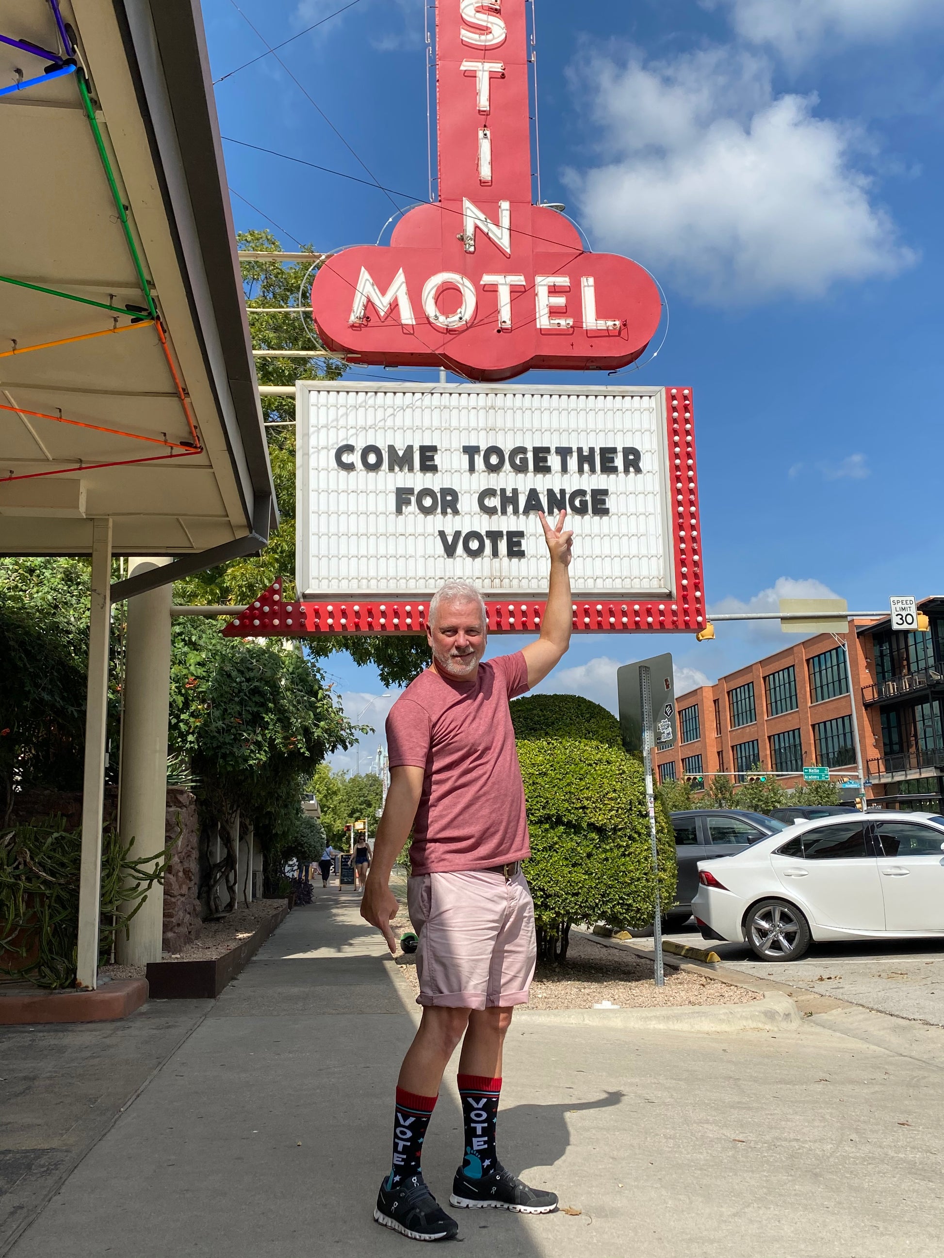 Middle-aged white haired man standing in front of Austin Motel in Austin, Texas modeling and wearing SoleMate Sox Midnight VOTE socks